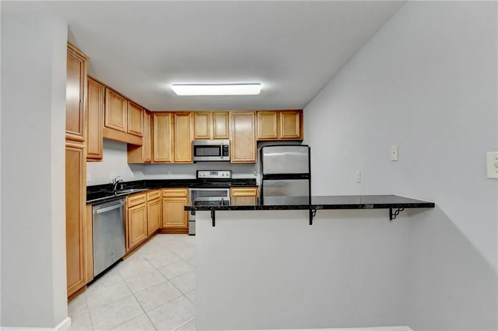 Kitchen featuring a kitchen breakfast bar, stainless steel appliances, a peninsula, dark stone countertops, and wood finish cabinetry
