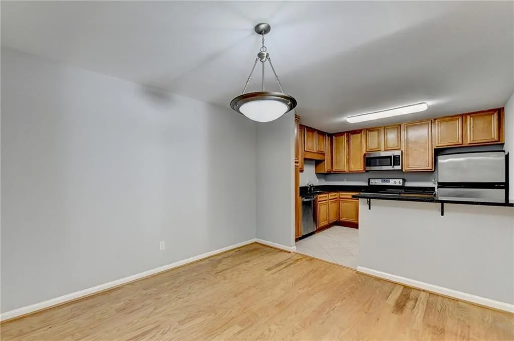 Kitchen featuring wood finish cabinetry, stainless steel appliances, light wood-type flooring, decorative light fixtures, and a breakfast bar