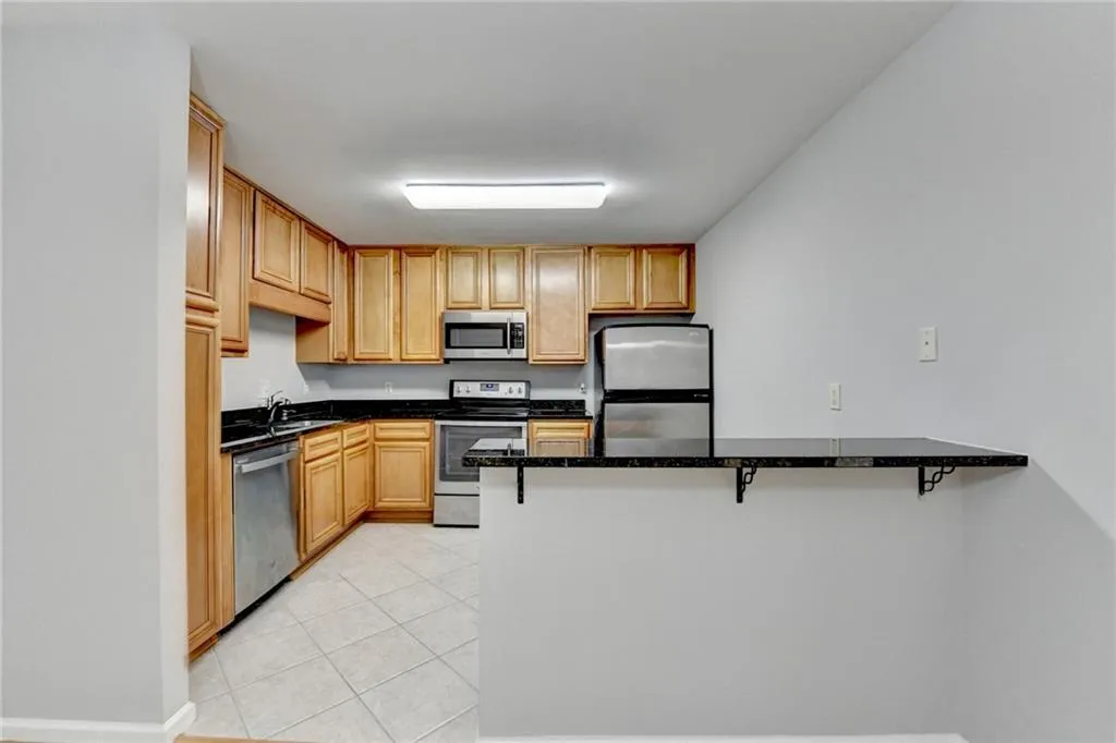Kitchen with stainless steel appliances, a peninsula, dark stone counters, a kitchen breakfast bar, and wood finish cabinets