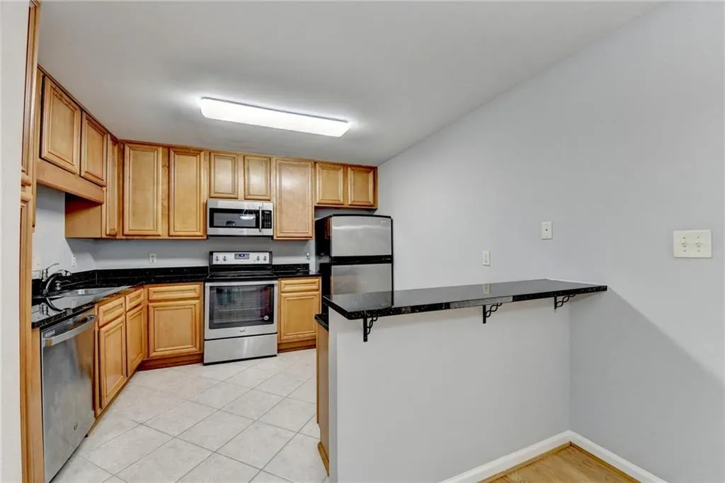 Kitchen with stainless steel appliances, a kitchen breakfast bar, a peninsula, dark stone countertops, and wood finish cabinets