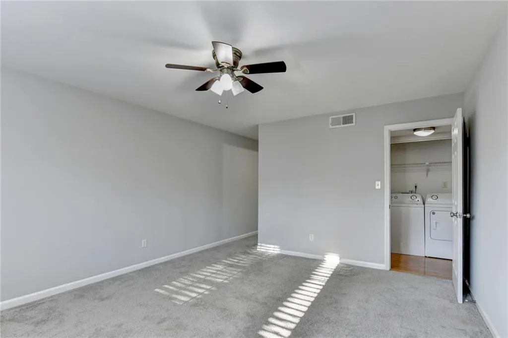 Unfurnished bedroom featuring washing machine and clothes dryer, light colored carpet, and ceiling fan