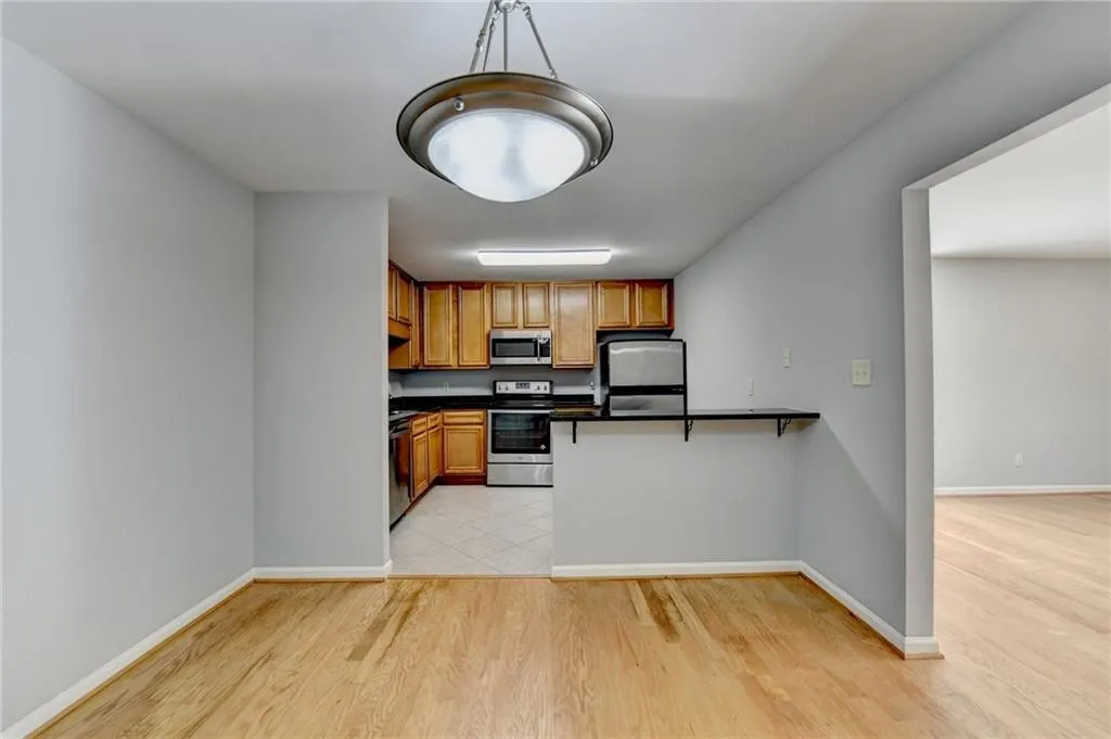 Kitchen with wood finish cabinetry, stainless steel appliances, a peninsula, decorative light fixtures, and light wood-style floors