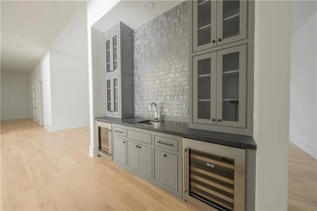 Bar featuring gray cabinets, sink, backsplash, and wine cooler