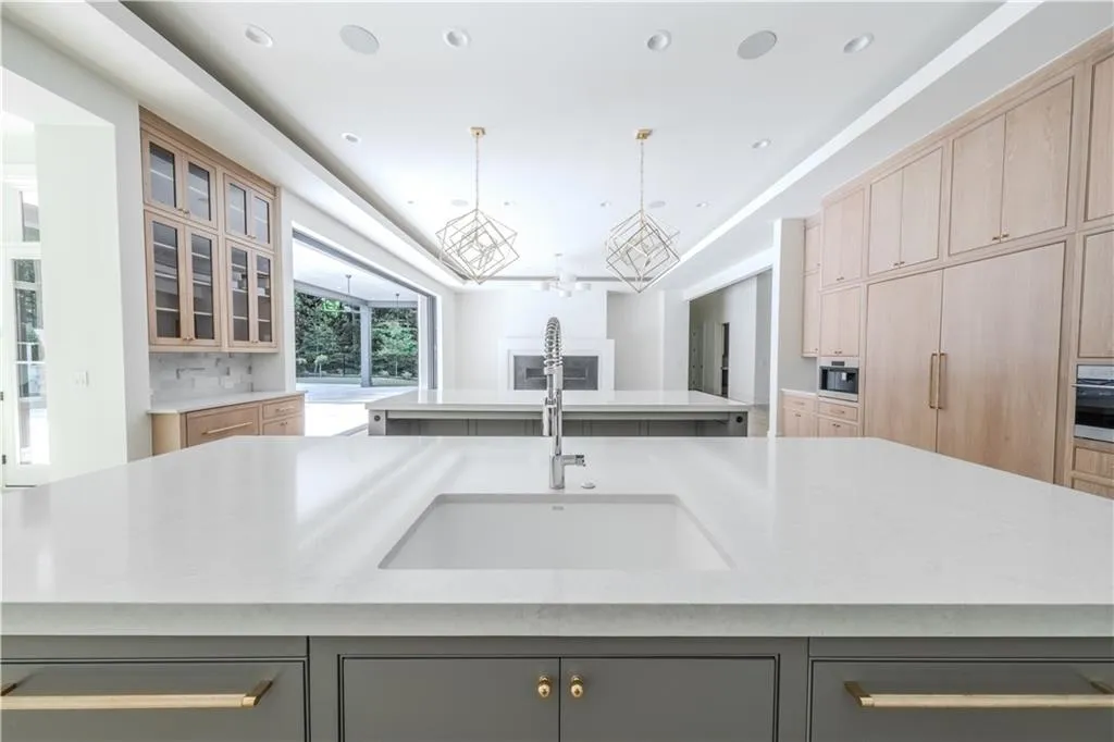 Kitchen with sink, light brown cabinets, hanging light fixtures, oven, and a spacious island