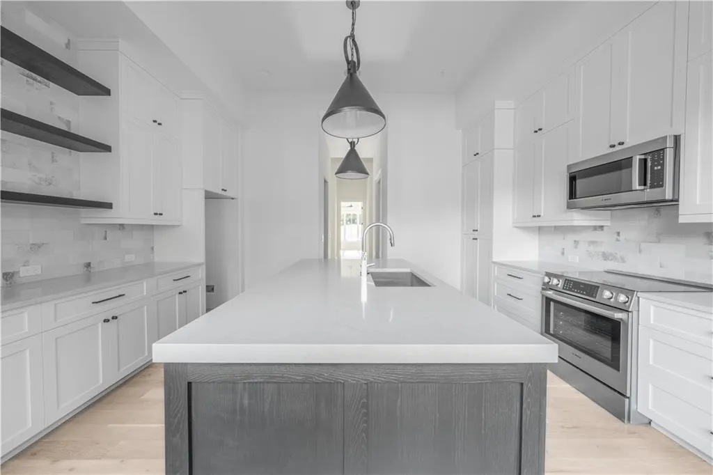 Kitchen with sink, decorative light fixtures, a center island with sink, white cabinets, and appliances with stainless steel finishes