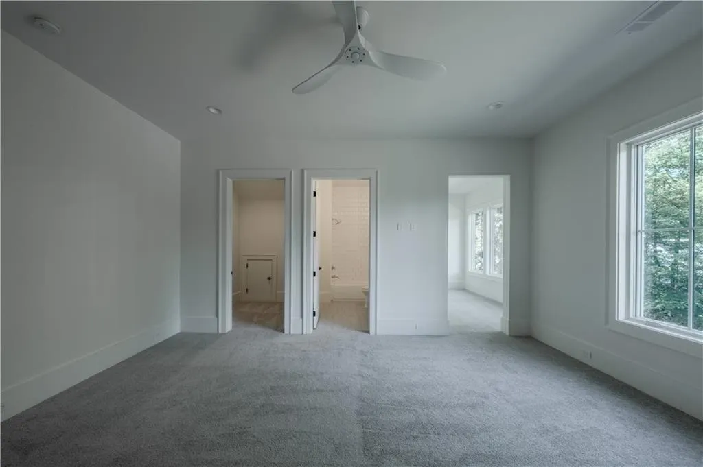 Unfurnished bedroom featuring connected bathroom, ceiling fan, and light colored carpet