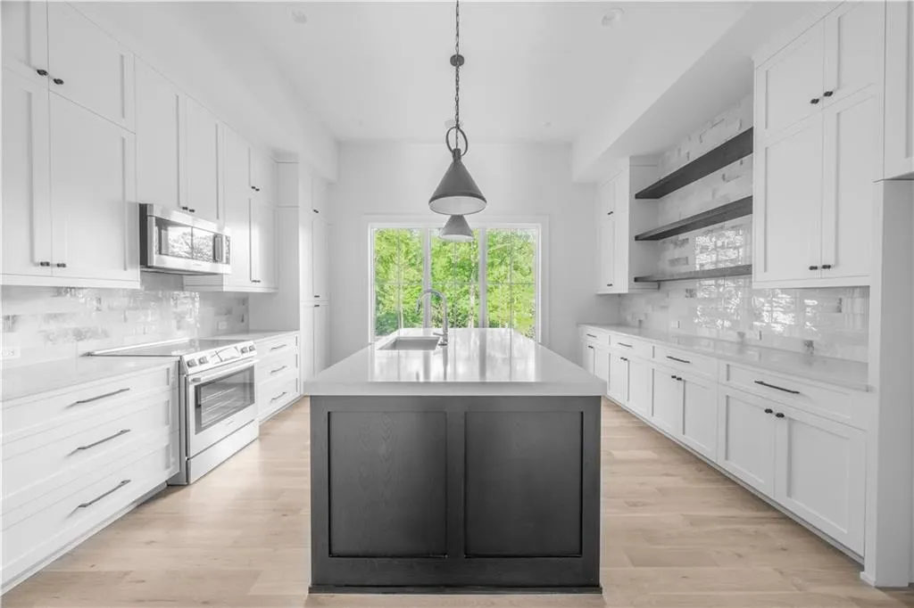 Kitchen with white cabinetry, an island with sink, and electric range oven