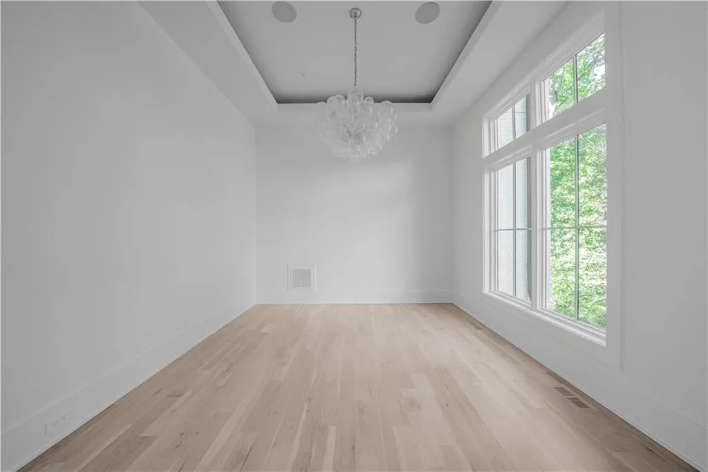 Spare room with a tray ceiling, an inviting chandelier, plenty of natural light, and light hardwood / wood-style floors