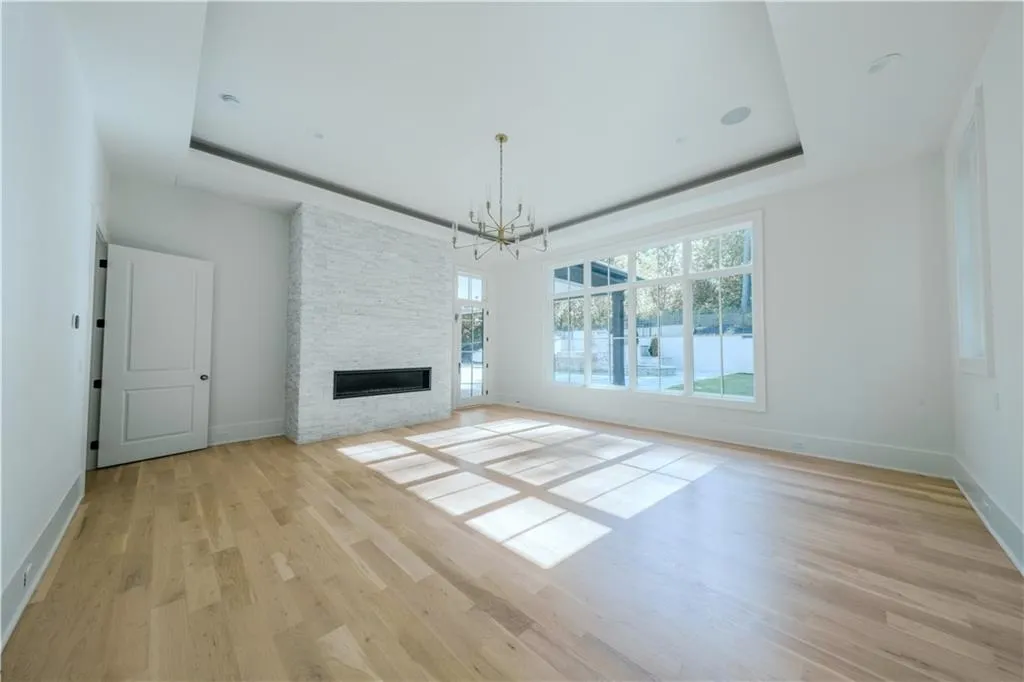 Unfurnished living room with a notable chandelier, a stone fireplace, a raised ceiling, and light hardwood / wood-style floors