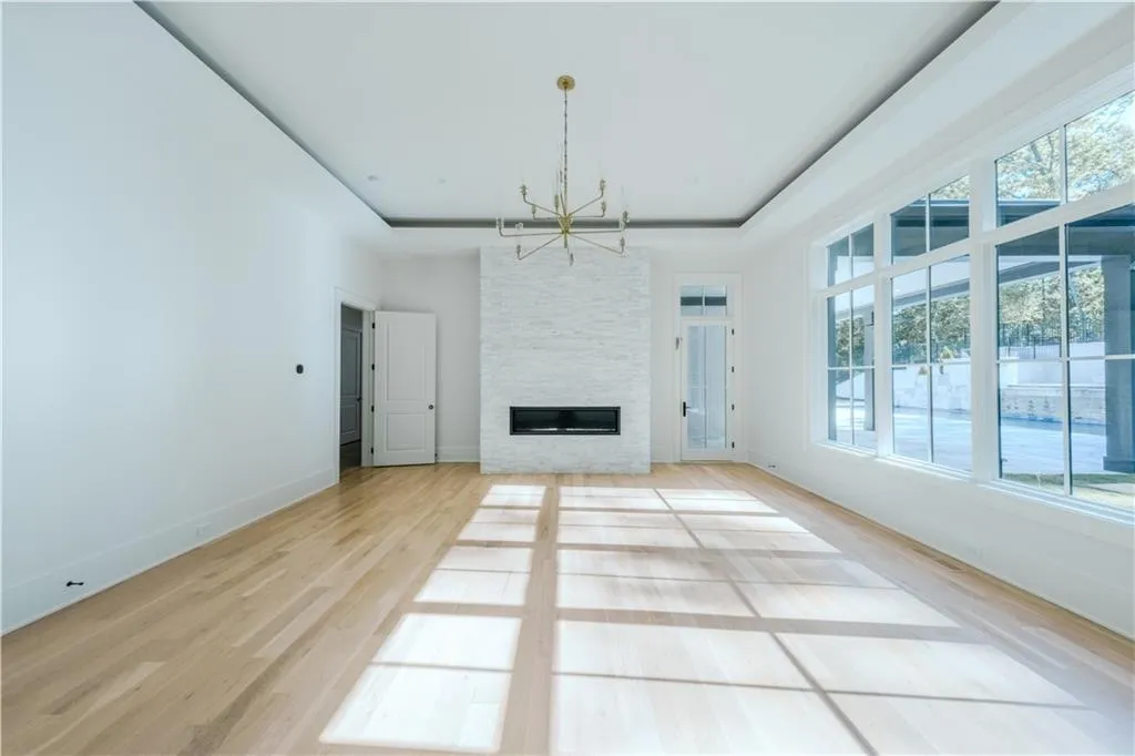 Unfurnished living room featuring a tray ceiling, a fireplace, a chandelier, and light hardwood / wood-style flooring