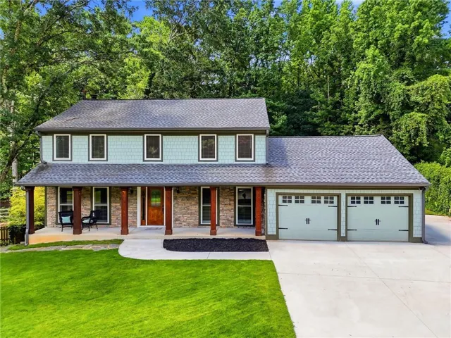 Two-story residence featuring a covered front porch with substantial pillars, a stone facade, and light blue shake siding