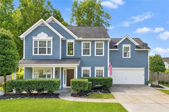 Blue siding exterior with white trim, a gabled roofline, an attached garage, a covered front porch, and a concrete driveway