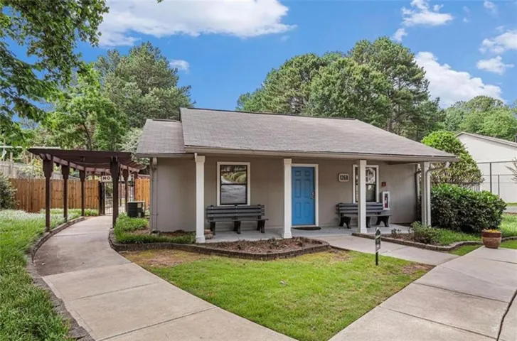 Single-story building featuring a prominent blue entry door, an extended wooden pergola, and a well-maintained concrete pathway