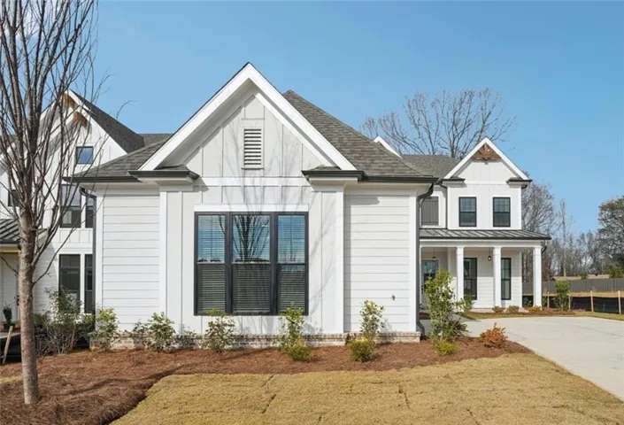 Modern farmhouse-style exterior featuring light-colored siding, dark-framed windows, a pitched roofline, white porch columns, and a concrete driveway