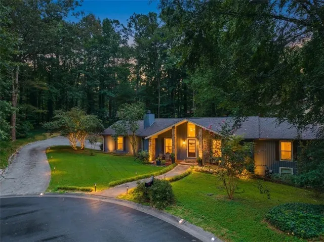 Wooded setting with a paved driveway, stone accents, and a well-maintained lawn