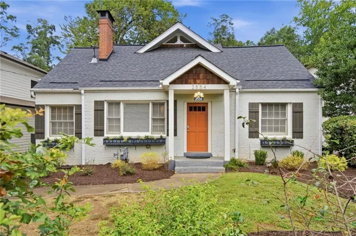 Gable roofline with dark shingles, light-colored brick exterior, and an orange entry door