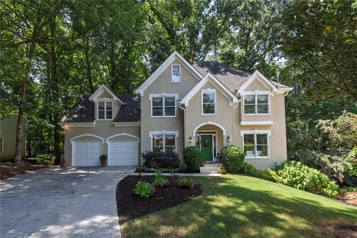 Stucco exterior with multiple gables and dormers, arched entryway, two-car garage, established front landscaping, and a sloped lawn