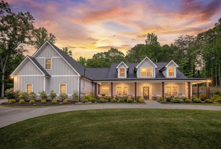 TWILIGHT Modern farmhouse exterior featuring board and batten siding, dormer windows, a covered front porch with timber posts, a concrete driveway, and mature landscaping