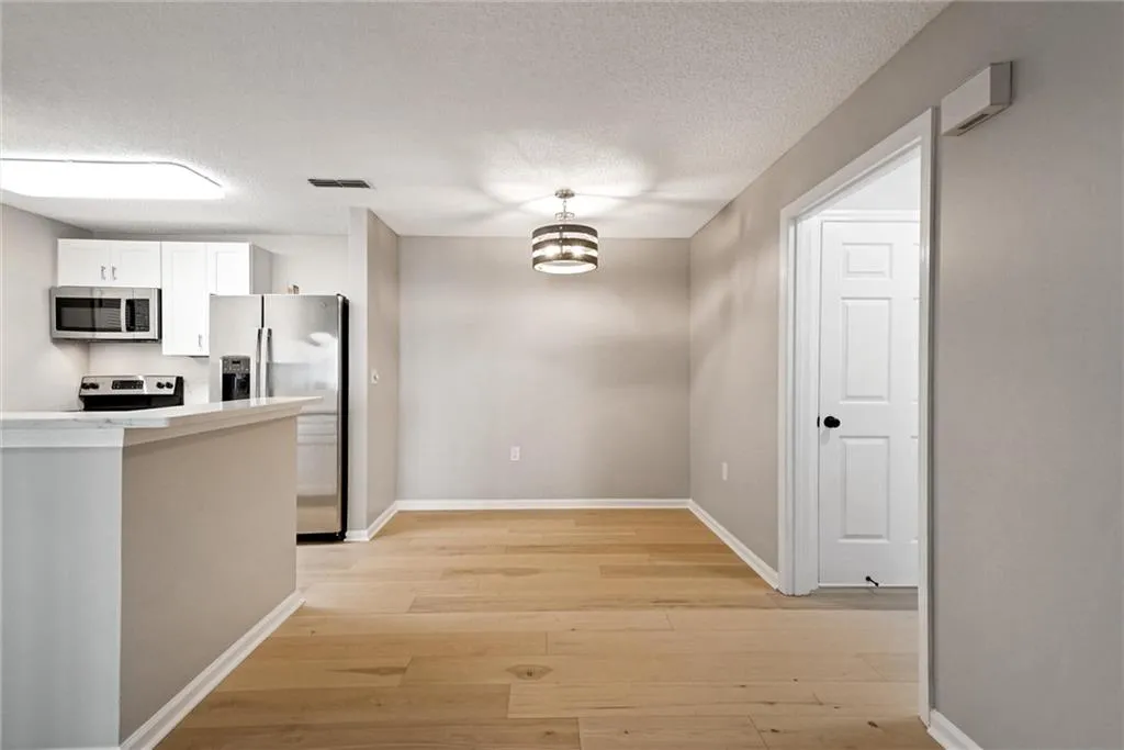Kitchen featuring white cabinetry, stainless steel appliances, light wood-style flooring, a chandelier, and a textured ceiling