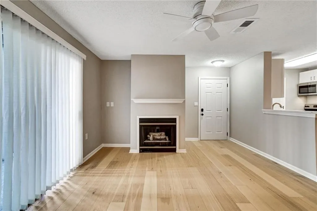Unfurnished living room with a textured ceiling, wood finished floors, ceiling fan, and a fireplace