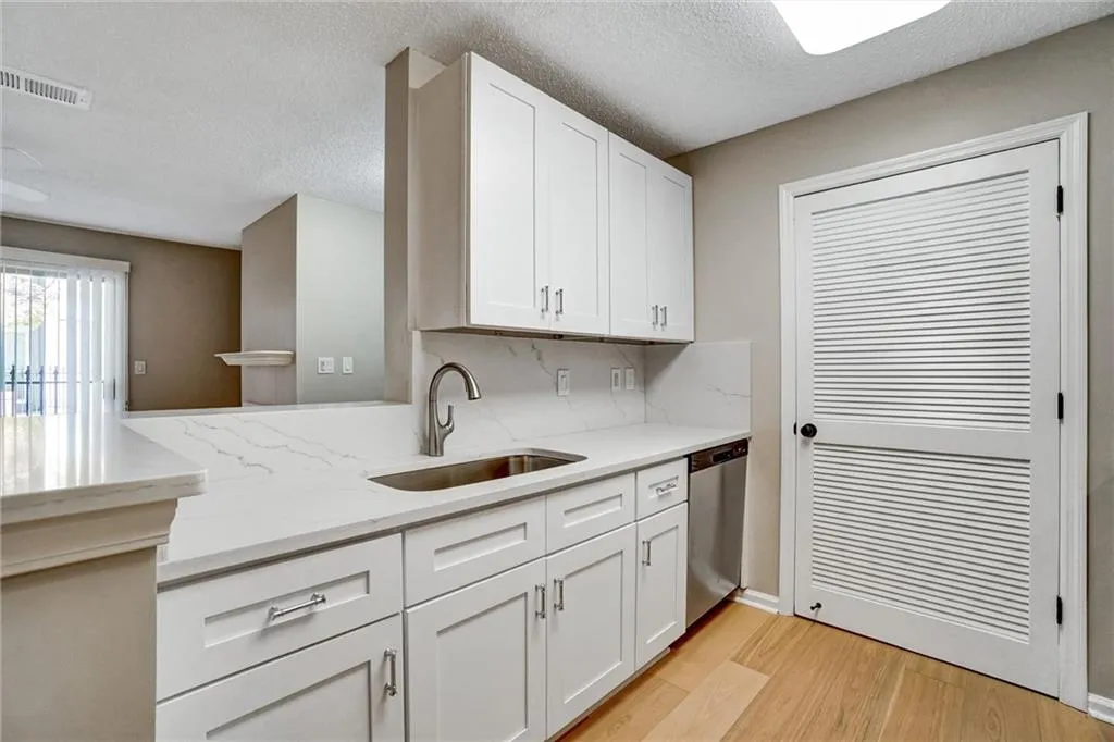 Kitchen featuring light wood-type flooring, white cabinets, light stone counters, a textured ceiling, and dishwasher