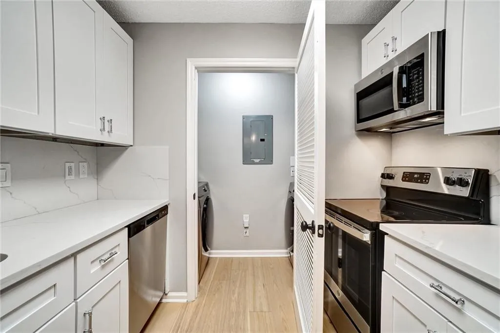 Kitchen featuring stainless steel appliances, white cabinets, light wood finished floors, electric panel, and a textured ceiling