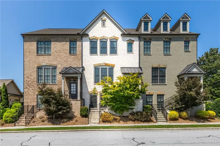 Brick and stucco exterior, prominent dormer windows, covered entryways, wrought iron railings, and mature landscaping