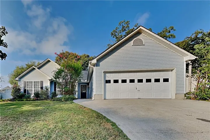 Light blue siding exterior with a white garage door, featuring a concrete driveway and an arched vent