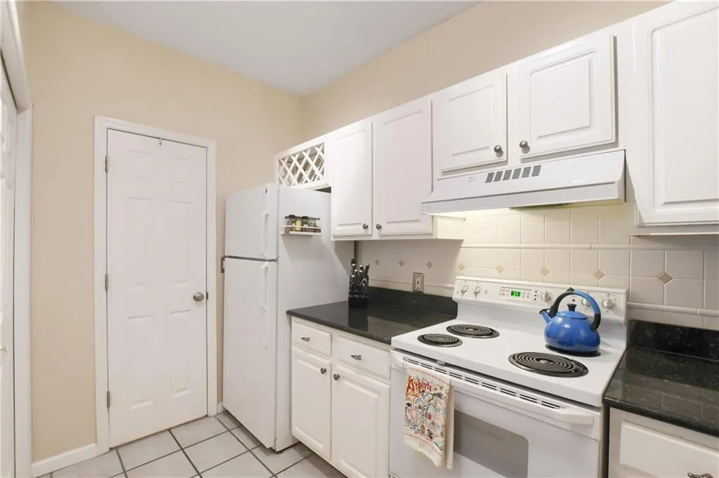 Kitchen featuring white appliances, decorative backsplash, under cabinet range hood, white cabinetry, and light tile patterned floors