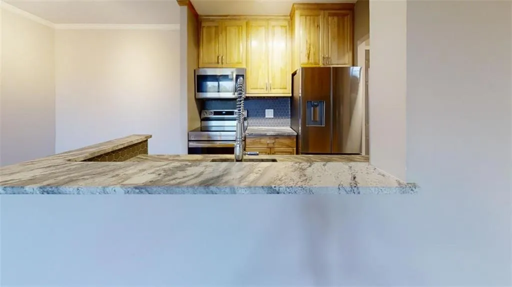 Kitchen featuring tasteful backsplash, light stone counters, crown molding, light brown cabinetry, and appliances with stainless steel finishes