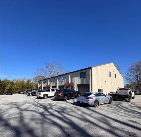 Commercial building featuring corrugated metal siding, multiple bay doors, upper-level windows, and a paved parking area
