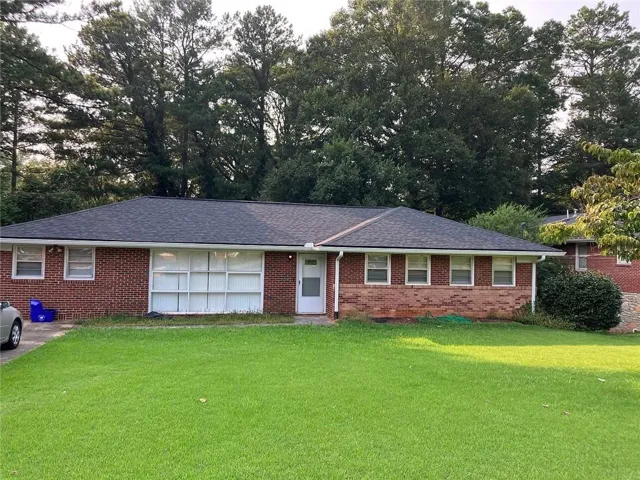 Brick exterior with a dark shingle roof, white front door, and a spacious green lawn