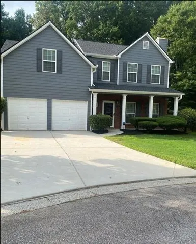Two-story residence featuring a two-car garage, gray siding, a covered porch with white columns, and brick accents