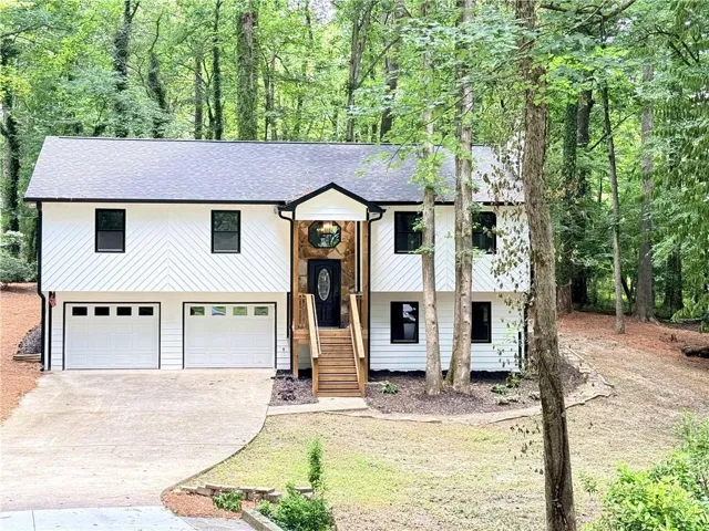 Split-level residence featuring white siding, black window frames, and a dark shingle roof