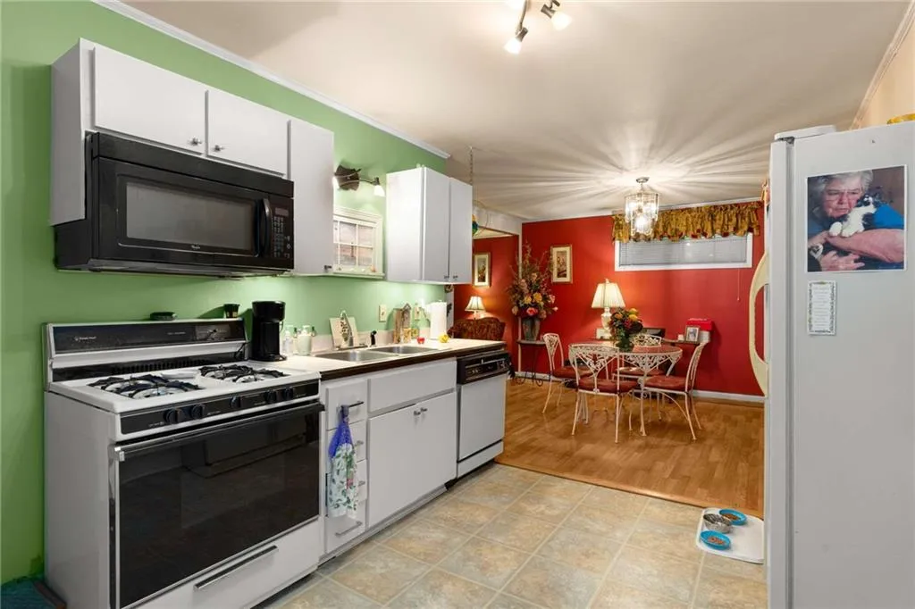 Kitchen with white appliances, white cabinetry, a chandelier, hanging light fixtures, and crown molding