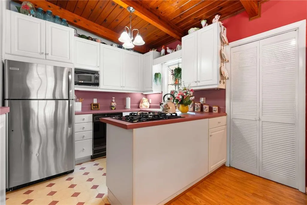 Kitchen featuring black appliances, a wooden ceiling with exposed beams, light floors, white cabinetry, and a peninsula