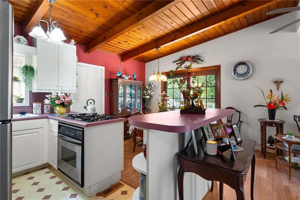 Kitchen featuring stainless steel oven, a chandelier, healthy amount of natural light, a wooden ceiling with exposed beams, and white cabinets