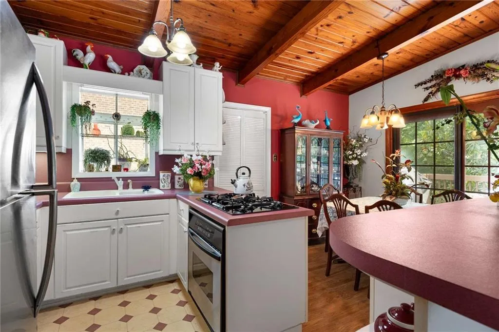 Kitchen with a chandelier, appliances with stainless steel finishes, a wood ceiling with exposed beams, light floors, and white cabinets