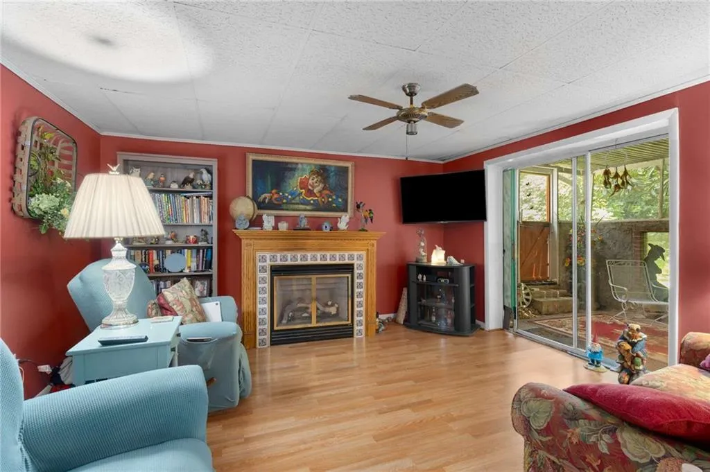 Living area with ceiling fan, wood finished floors, a tile fireplace, and crown molding