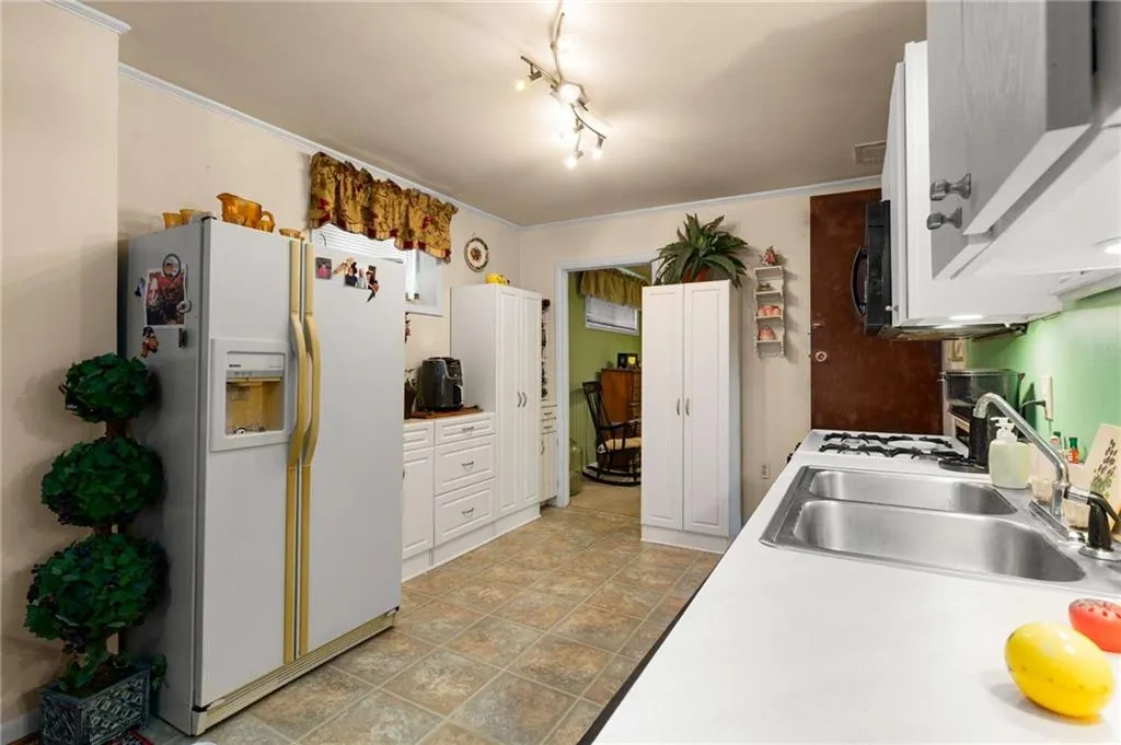 Kitchen featuring white refrigerator with ice dispenser, black microwave, white cabinetry, light countertops, and ornamental molding
