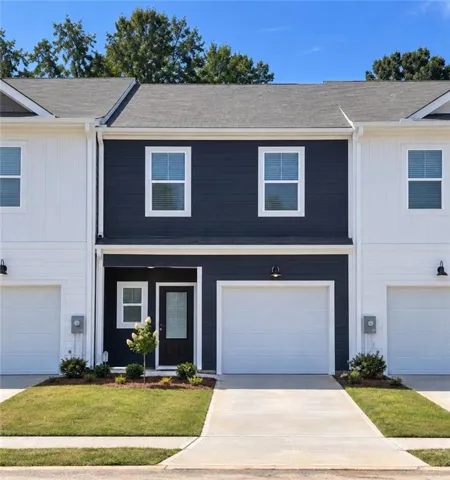 Contemporary townhome exterior featuring a contrasting dark and light facade, individual garage, front entry door with a transom window, and a landscaped front yard