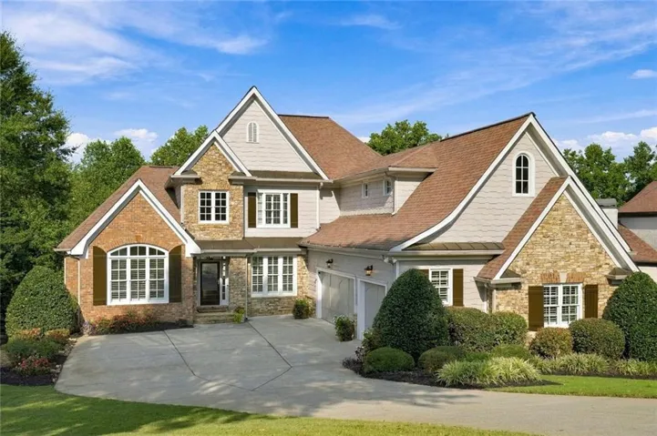 Multi-gabled exterior featuring a blend of brick and stone accents, a multi-pane arched window, an attached three car garage, and a concrete driveway