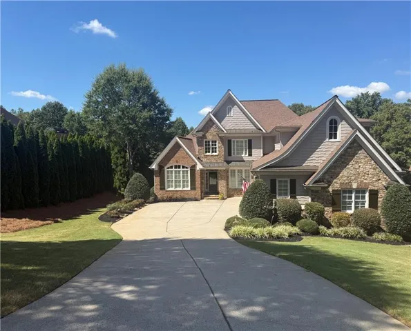 Exterior featuring brick and stone veneer accents, multi-pane windows with dark shutters, gabled rooflines, and a concrete driveway