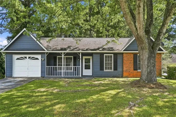 Exterior featuring blue siding, brick accents, a white garage door, and a covered front porch with white railing