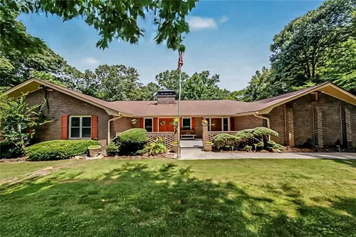 Classic four-sided brick ranch with mature landscaping, a welcoming covered porch, and a spacious front yard shaded by established trees.