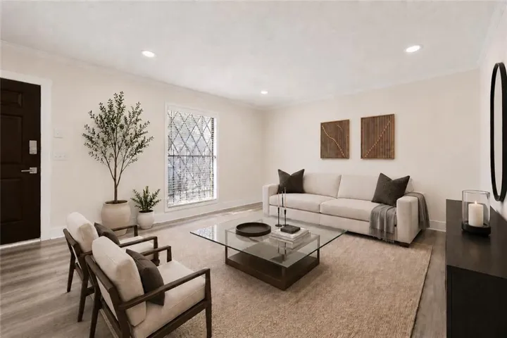 Recessed ceiling lighting, wood-finish flooring, crown molding, a large window with blinds, and a dark paneled entry door