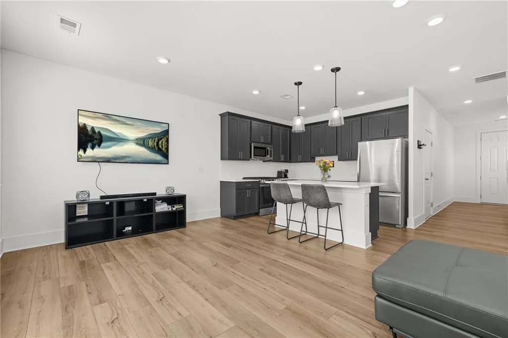 Living room and with a kitchen bar, stainless steel appliances, light wood-type flooring, a kitchen island, and decorative light fixtures