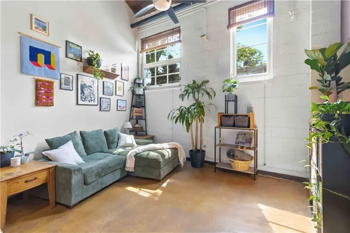 Living room featuring plenty of natural light, finished concrete flooring, ceiling fan, and concrete block wall