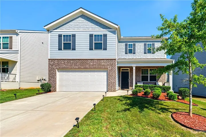 Two-story residence featuring a brick and siding exterior, an attached garage, a covered front entry, a concrete driveway, and established landscaping