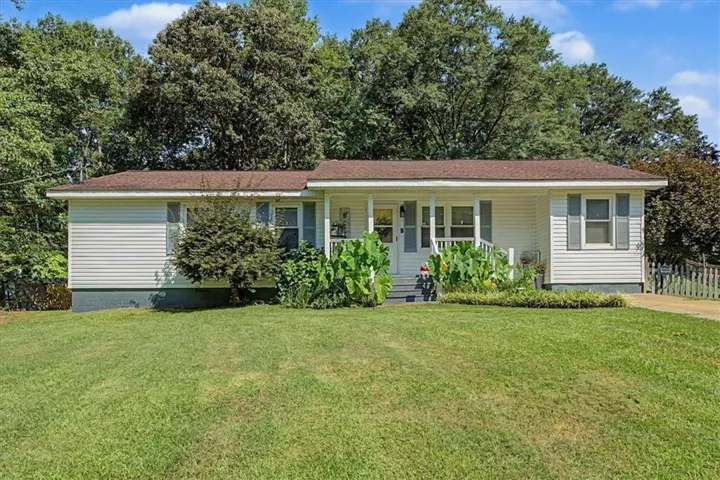 White siding exterior with a covered porch, front yard, and mature trees